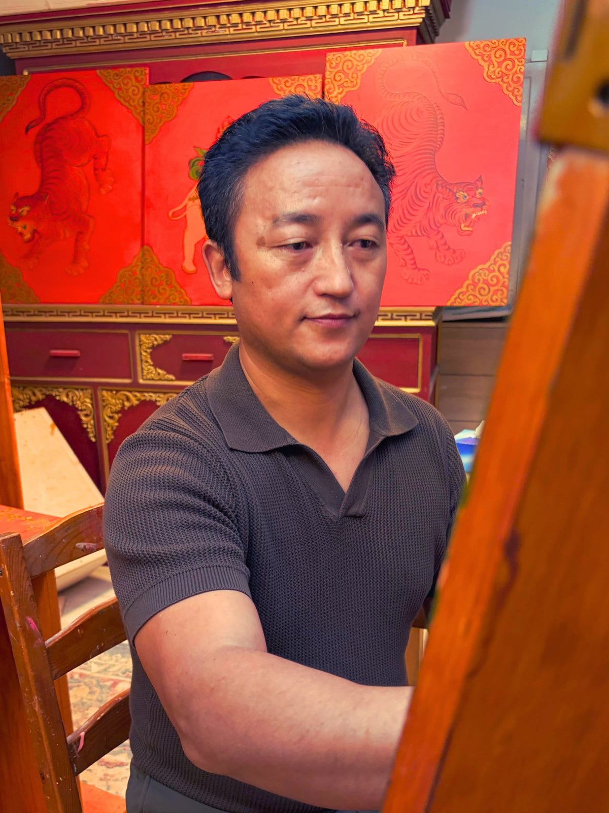 Jamyang an der Staffelei, hinter ihm bemalte Möbel mit Tigermotiven